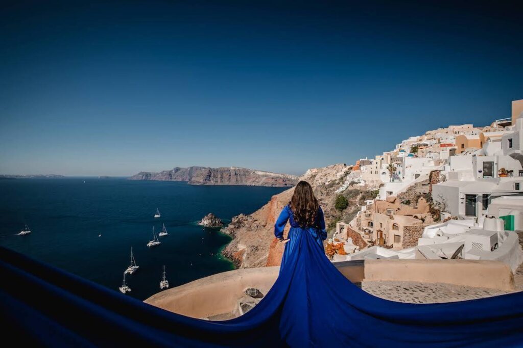 Rachel Rofé wearing a blue dress overlooking the ocean, mountains, and houses.